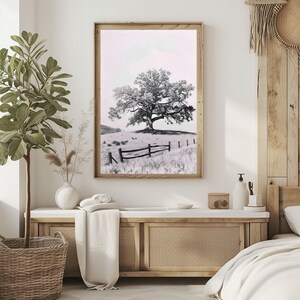 May include: A black and white photograph of a lone tree in a field with a wooden fence. The tree is in the center of the image and the fence is in the foreground. The background is a soft, blurred landscape.