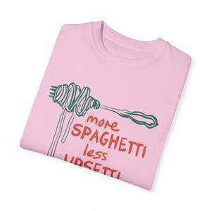 May include: Pink t-shirt with a green and white illustration of spaghetti on a fork. The text "more spaghetti less upset" is printed in red on the shirt.