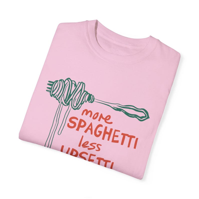 May include: Pink t-shirt with a green and white illustration of spaghetti on a fork. The text "more spaghetti less upset" is printed in red on the shirt.
