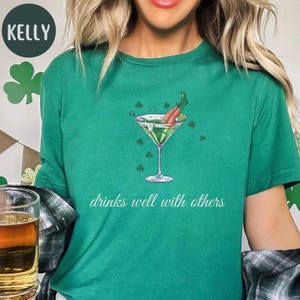May include: Green t-shirt with a green martini glass with two carrot sticks in it. The text "drinks well with others" is printed below the glass.