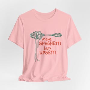 May include: Pink t-shirt with a green and red illustration of spaghetti on a fork and the text "more spaghetti less upsetti"