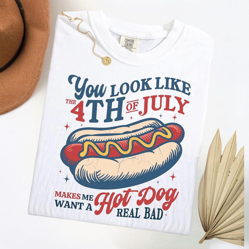 K&ouml;nnte beinhalten: Wei&szlig;es T-Shirt mit einem Hotdog-Motiv und dem Text "You look like the 4th of July makes me want a hot dog real bad." Der Hotdog ist rot mit gelbem Senf.