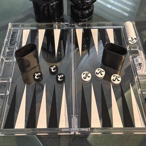 May include: A clear acrylic backgammon set with black and white playing surface. Includes black leather dice cups, dice, and playing pieces. The game board is open and ready for play.