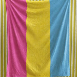 Pode incluir: Um tecido listrado rosa, amarelo e azul pendurado em uma parede.