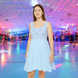 Op de afbeelding: Een lichtblauwe skaterjurk met een patroon van roze, witte en blauwe vlinders. De jurk is mouwloos en heeft een ronde hals. Het model draagt de jurk in een rolbaan.