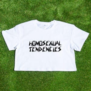 May include: White crop top with black text that reads "HOMOSEXUAL TENDENCIES".