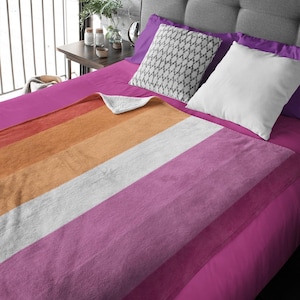 Könnte beinhalten: Eine weiche, flauschige Kuscheldecke mit einem Design der lesbischen Pride-Flagge. Die Decke hat Streifen in Orange, Pfirsich, Weiß, Rosa und Lavendel.