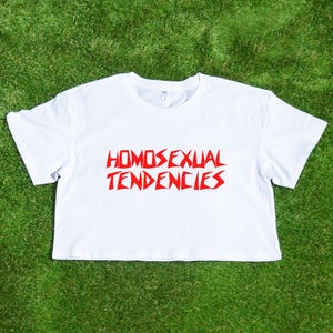 May include: White cropped t-shirt with red text that reads "HOMOSEXUAL TENDENCIES" in a jagged font.
