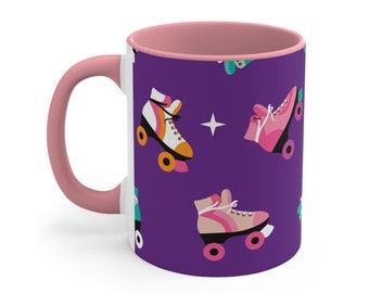 May include: A white ceramic mug with a pink handle and rim. The mug features a purple background with a repeating pattern of colorful roller skates.