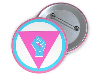 May include: A pink and blue button with a raised white circle and a pink triangle with a blue fist inside. The button has a silver back with a safety pin.