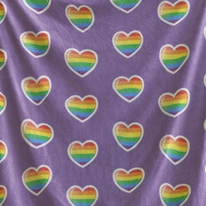 Könnte beinhalten: Lilafarbene Fleece-Decke mit einem sich wiederholenden Muster aus Regenbogenherzen.