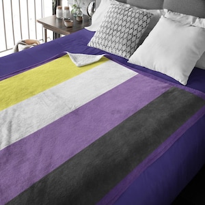 May include: A soft, plush blanket with stripes of yellow, white, purple, and black. The blanket is folded on a bed with a blue sheet.