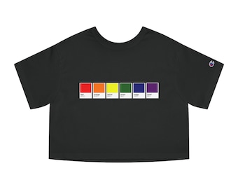 Può includere: Maglietta nera a maniche corte e a taglio crop con una grafica a palette di colori arcobaleno. La grafica presenta una fila di campioni di colore etichettati con i colori: rosso, arancione, giallo, verde, indaco e viola.