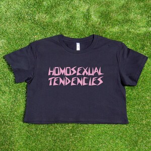 May include: A black cropped t-shirt with the phrase "HOMOSEXUAL TENDENCIES" printed in pink letters.
