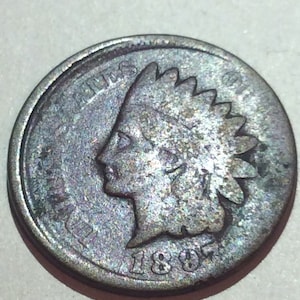 May include: An antique Indian Head penny from 1897. The coin features a profile of a Native American in a feathered headdress. The coin is a copper color with signs of wear and age.