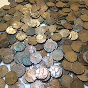May include: A large pile of copper pennies, some with visible dates and portraits. The coins vary in color from shiny copper to dark brown and green due to oxidation. Some pennies have holes or are damaged.