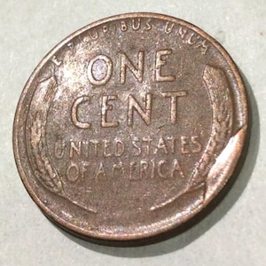 May include: A close-up of a copper-colored United States one-cent coin. The coin features the words "ONE CENT" in large capital letters, with "UNITED STATES OF AMERICA" below. The coin's rim is slightly worn.