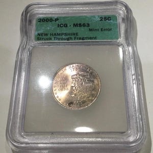 May include: A 2000-P New Hampshire quarter coin, encapsulated in a clear plastic case. The coin has a mint error and is graded MS63 by ICG. The coin's face features text and an image of a historical scene.