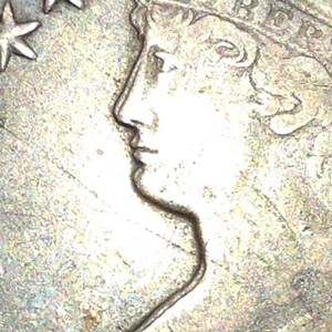 May include: Close-up of a silver coin featuring a profile of a woman's face, wearing a crown. The coin has a star and the word "Liberty" is visible. The coin is likely a collectible or historical item.