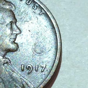 May include: Close-up of a well-worn coin, featuring a profile of a man and the year 1917. The word "TRUST" is visible at the top. The coin has a silver and bronze color.