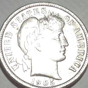 May include: A silver coin from 1905, featuring a profile of a person and the words "UNITED STATES OF AMERICA." The coin has a detailed edge and is slightly worn, showing signs of age.
