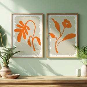 Puede incluir: Dos impresiones enmarcadas con diseños florales naranjas sobre un fondo beige. Las impresiones están colgadas en una pared verde claro sobre un estante de madera con dos jarrones y un cuenco.
