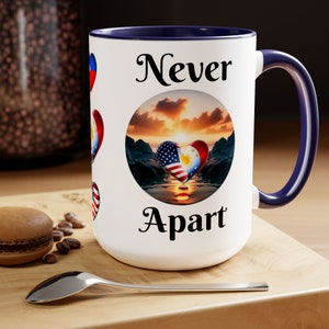 Può includere: Tazza in ceramica bianca con interno e manico blu navy. La tazza presenta un design a cuore con le bandiere americana e filippina e le parole "Never Apart". Ulteriori disegni a cuore con bandiere sono sul lato.