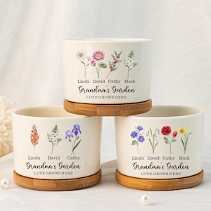May include: Three white ceramic flower pots with a bamboo base. Each pot features a floral design and the text "Grandma's Garden, Love Grows Here". The pots are labelled with the names Linda, David, Cathy, and Mark.