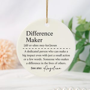 May include: White ceramic bauble with the word "Difference Maker" defined as "A dedicated person who can make a big impact even with just a small action or a few words. Someone who makes a difference in the lives of others." The bauble also includes the text "See also: Angelina".