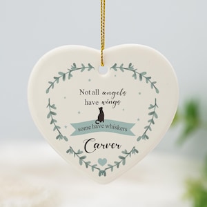 Op de afbeelding: Witte, hartvormige keramische hanger met een groene krans van bladeren en de tekst "Not all angels have wings, some have whiskers" met een zwart katten silhouet. De naam "Carver" staat onder de tekst.