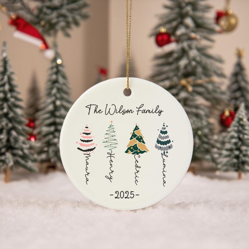 May include: A round white ceramic Christmas ornament hanging from a gold string. It features the text The Wilson Family, the year 2025, and four stylized Christmas tree illustrations with the names Maura, Henry, Cedric, and Lumina below.