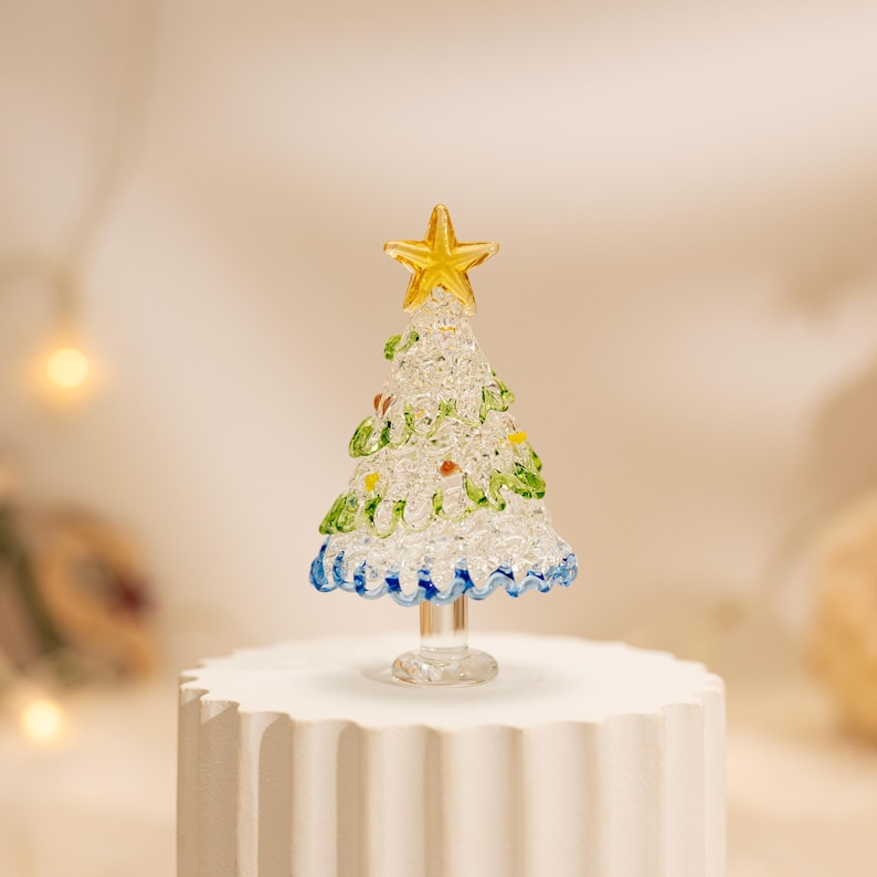 Op de afbeelding: Een kerstboomfiguur van helder glas met een getextureerd, kristallijn oppervlak met groene glazen accenten en kleine kleurrijke stippen. De boom is bekroond met een gele glazen ster en staat op een heldere glazen voet.