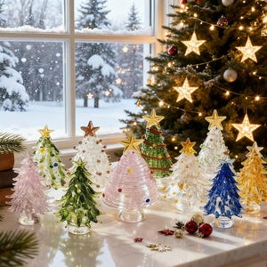 Op de afbeelding: Een verzameling kleine, decoratieve kerstboompjes van glas in diverse kleuren zoals roze, groen, blauw, geel en transparant, elk bekroond met een gouden ster. De boompjes hebben geribbelde oppervlakken en staan opgesteld op een witte ondergrond.