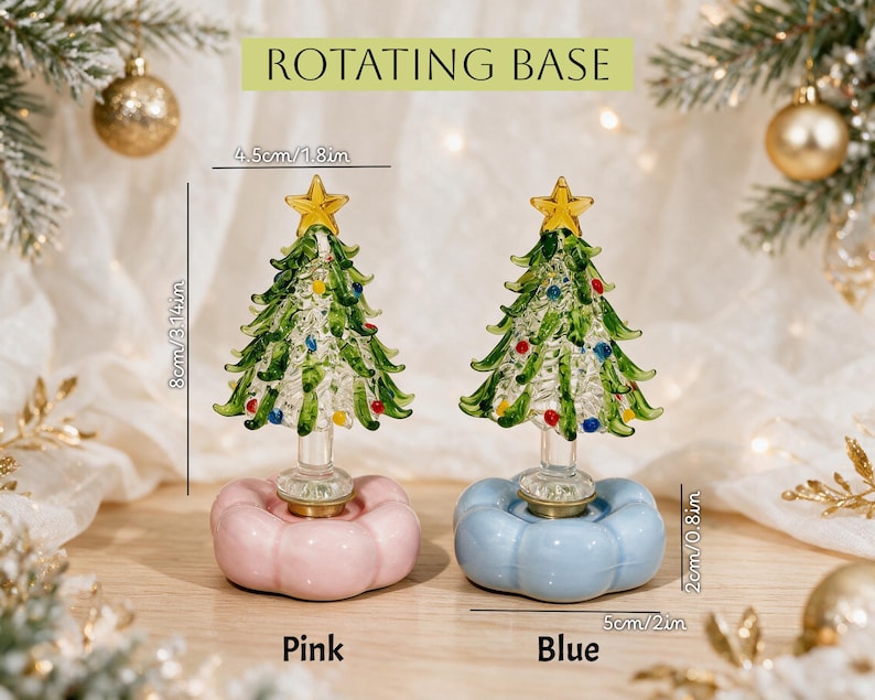 Op de afbeelding: Twee glazen kerstboomornamenten met gele sterren als piek, groene takken en kleurrijke accenten. Elke boom staat op een draaibare voet, &eacute;&eacute;n roze en &eacute;&eacute;n blauw. De bomen zijn 8 cm hoog en 4,5 cm breed, met voetstukken van 2 cm hoog en 5 cm breed.