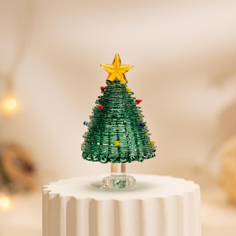 Op de afbeelding: Een miniatuur kerstboomfiguur van glas met een conisch groen lichaam met spiraalvormige glasstructuur, versierd met kleine veelkleurige glaskralen als ornamenten en bekroond met een gele glasster op een doorzichtige glazen voet.