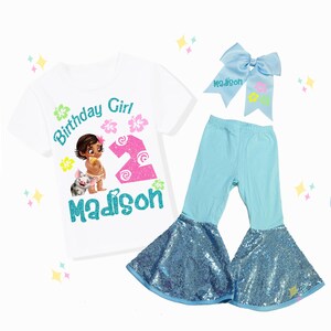 May include: A white t-shirt with a graphic of a cartoon girl, pig, and the text "Birthday Girl", "2", and "Madison". The outfit includes light blue pants with sequin flares and a matching bow.
