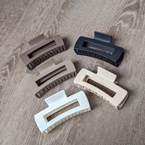 Puede incluir: Cuatro pinzas para el pelo de diferentes colores: marrón, negro, beige y blanco. Las pinzas son de plástico y tienen una forma curva con una abertura rectangular en el medio.