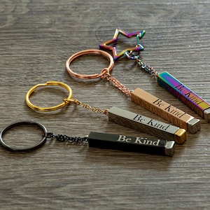 May include: Four keychains with a star charm and a rotating cylinder with the words "Be Kind" engraved on each. The keychains are silver, gold, black, and rainbow.
