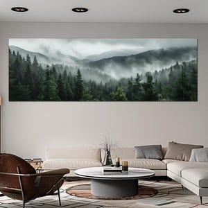 May include: A panoramic canvas print of a misty forest scene. The artwork depicts a lush green forest with tall trees and rolling hills shrouded in fog. The artwork is mounted on a white wall above a modern living room.