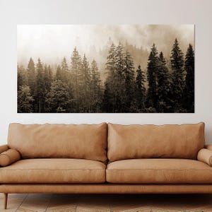 May include: Sepia-toned canvas art print depicting a misty forest scene. The image features tall evergreen trees, with a soft, diffused light creating depth. The artwork is displayed above a brown leather sofa.