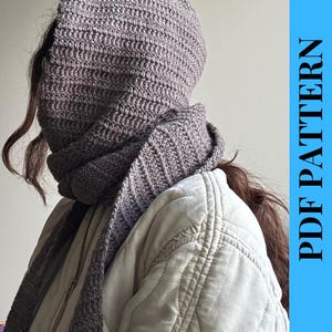 Op de afbeelding: Een gehaakte capuchon- en sjaalset in een gedempte grijze kleur. De capuchon bedekt het hoofd en de nek, met de sjaal om de nek gedrapeerd. De tekst "PDF PATTERN" is verticaal op een blauwe achtergrond gedrukt.