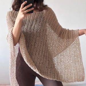 May include: A beige, open-weave poncho with a square neckline and wide sleeves. The poncho is made of a light, airy material, perfect for layering. The garment drapes loosely, offering a relaxed fit. The overall style is casual and bohemian.