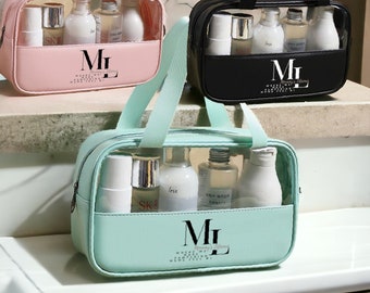 Puede incluir: Tres bolsas de viaje de plástico transparente con cremalleras y asas negras. Las bolsas están llenas de varios frascos de artículos de tocador. Las bolsas son de color rosa, negro y verde claro. Las bolsas tienen el texto "ML" en la parte delantera.