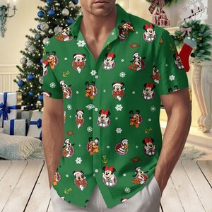 May include: A green short-sleeved button-down shirt featuring a repeating pattern of Disney characters including Mickey Mouse, Minnie Mouse, Pluto, and Goofy wearing Santa hats, interspersed with white snowflakes and small gold anchors.