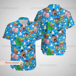Könnte beinhalten: Ein blaues, kurzärmeliges Hemd mit Knöpfen und einem sich wiederholenden Muster von Toy Story-Charakteren, darunter Woody, Buzz Lightyear, Rex und Mr. Potato Head. Die Figuren sind von Sternen und Wolken umgeben. Das Hemd hat einen Kragen und eine Knopfleiste.