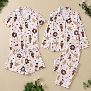 May include: Two sets of white pajamas featuring a repeating Christmas pattern of nutcrackers, gingerbread men, wreaths, candy canes, and red hearts. One set includes a short-sleeve button-down shirt and shorts, while the other has a long-sleeve shirt and pants.