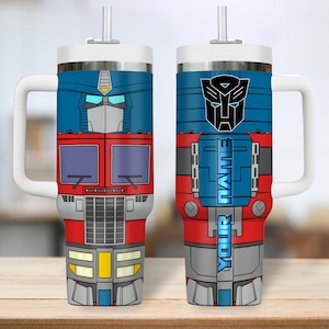 May include: A double-walled tumbler featuring a design of Optimus Prime from Transformers. The tumbler has a white handle and lid, a straw, and a design that includes the Autobot symbol and the text "YOUR NAME". The tumbler is red, blue, gray, and yellow.