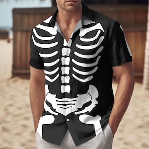 Puede incluir: Camisa negra de manga corta con un diseño de esqueleto blanco. La camisa tiene un cuello clásico y un estampado de esqueleto completo en la parte delantera. Prenda con temática de Halloween.