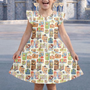 May include: A sleeveless, cream-colored dress featuring a repeating pattern of colorful Muppet characters. The dress has a round neckline and ruffled sleeves. The skirt flares out from the waist, creating a playful silhouette. The background is blurred, suggesting an outdoor setting.