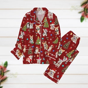 May include: Red Christmas pajamas set featuring a pattern of corgi dogs wearing Santa hats and scarves, along with Christmas trees and ornaments. The long-sleeved top and pants have white trim.